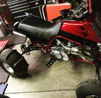 Red mini dirt bike with black seat in a garage, showing chrome engine and wheels.