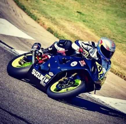 Motorcyclist leaning hard into a turn on a blue Suzuki racing bike on a track
