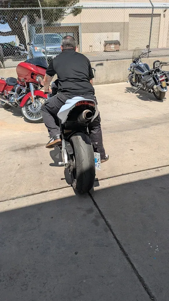 Person on a black sport motorcycle in a parking lot, with red and black motorcycles nearby.