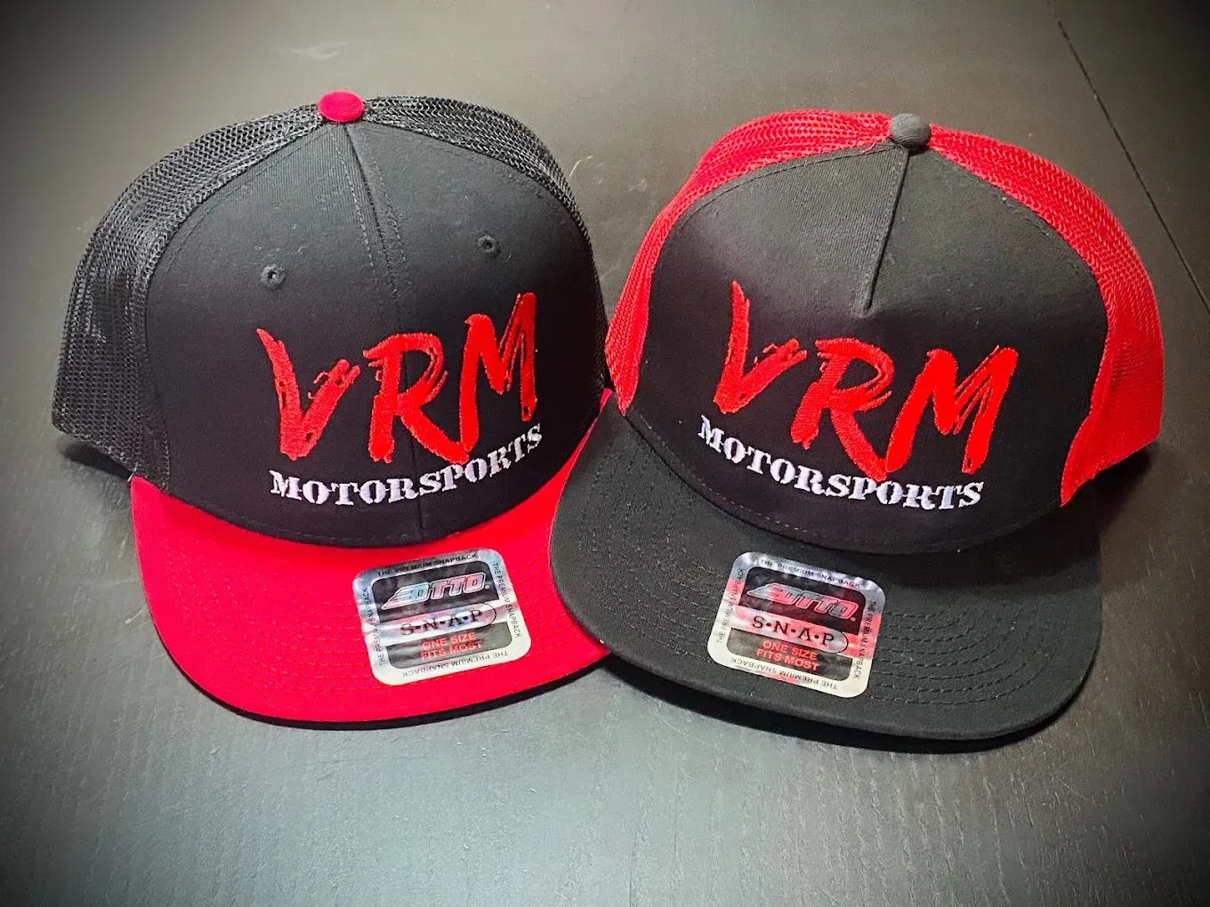 Two black and red VRM Motorsports caps on a dark surface