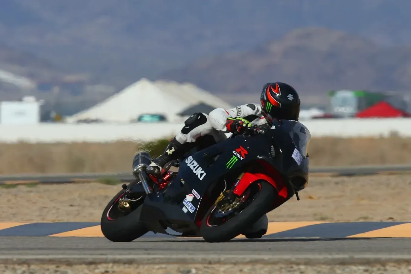 Motorcycle racer leaning into a turn on a racetrack, wearing black-and-red gear and helmet.