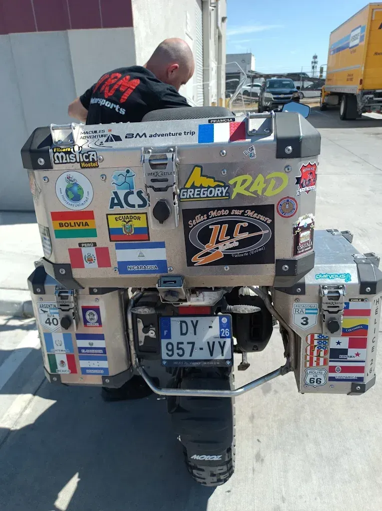 Sticker-covered motorcycle parked outdoors beside a truck, with a person leaning over the seat.